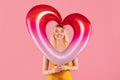 Smiling blonde woman with heart-shaped balloon on pink background Royalty Free Stock Photo