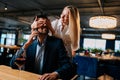 Joyful blonde young woman closed eyes of surprised elegant man in suit sitting at table with glass red wine talking on Royalty Free Stock Photo