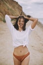 Joyful boho girl in white shirt having fun on sunny beach. Carefree stylish woman in swimsuit and shirt smiling and relaxing on