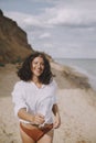 Joyful boho girl in white shirt running on sunny beach. Carefree stylish woman in swimsuit and shirt relaxing on seashore. Summer