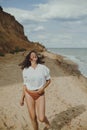 Joyful boho girl in white shirt running on sunny beach. Carefree stylish woman in swimsuit and shirt relaxing on seashore. Summer