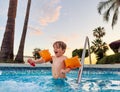 Joyful boy in arm bands enjoying sunset swimming pool Royalty Free Stock Photo