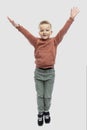 Joyful boy with his hands up. The guy in jeans and a brown sweater. Positiveness and happiness. Isolated on a light gray