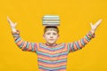 A joyful boy holds a bundle of textbooks on his head and holds his hands at the sides