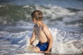 Joyful boy near the sea plays with the waves.