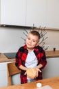 A joyful boy at a wooden table in the kitchen making cookies with cookie cutter in a shape of little Christmas tree Royalty Free Stock Photo