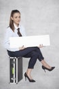 Joyful business woman sits on a suitcase and holds a commercial