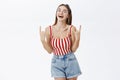 Joyful carefree stylish pinup girlfriend in striped top and denim shorts showing rock n roll gesture laughing amused