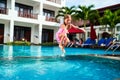 Excited young girl in pink swimsuit leaps into azure pool at sunny resort. Joyful child enjoying summer splash, vacation Royalty Free Stock Photo