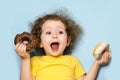 Joyful child screams with happiness. emotional girl eating tasty donuts with chocolate and white icing. trend in food, sweets for