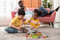 Joyful children sitting on carpet floor and playing with colorful wooden building blocks while parents relaxing on couch with Royalty Free Stock Photo