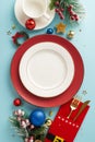Vertical top-down view featuring plates, whimsical cutlery holder, mug, balls, confetti, frosted fir, holly berries on blue