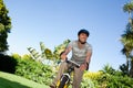 Mid-adult man riding bicycle wearing striped polo shirt and helmet along tropical garden pathway Royalty Free Stock Photo
