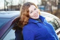 Joyful curly hair woman leaned against car
