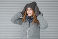 Joyful cute young woman in a gray knitted hat in a stylish gray coat with fur in knitted vintage mittens with a beautiful smile