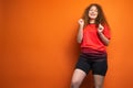 Joyful dancing redhead woman in favourite football team uniform posing on orange background, football fan emotions Royalty Free Stock Photo