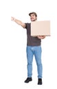 Joyful delivery man, full length portrait, carrying a cardboard parcel box pointing his index finger ahead, isolated on white.