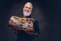 Joyful elderly butcher with apron holding huge meat piece