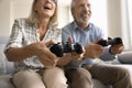 Joyful elderly husband and wife pushing buttons on gamepads