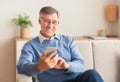 Joyful Elderly Man Using Cellphone Sitting On Sofa At Home Royalty Free Stock Photo