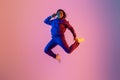 Joyful energetic black woman in sportswear having fun and jumping high on neon colorful studio background, full length