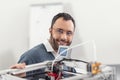 Joyful engineer in eyeglasses posing near 3D printer