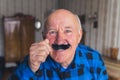 joyful European senior man with blue eyes and fake moustache medium closeup indoors seniority concept