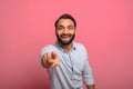 Joyful excited Indian middle-aged man in jeans shirt points fingers at the camera