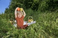 nice and funny fair-haired kid holds an apple and orange, basket with fruits on green grass Royalty Free Stock Photo