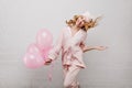 Joyful fair-haired girl posing with tongue out and holding bunch of pink balloons. Indoor portrait of ecstatic curly