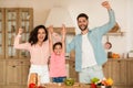 Joyful family holding hands and shaking fists, gesturing yes while preparing dinner together in kitchen Royalty Free Stock Photo