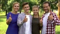 Joyful family members enjoying weekend in park and showing thumbs up into camera Royalty Free Stock Photo