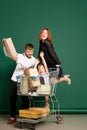 Joyful family, mother, father and son with shopping bags and boxes ride on shop cart isolated on green background Royalty Free Stock Photo