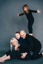 Joyful family mother, father and two little children in black clothes having fun on floor with dark background Royalty Free Stock Photo