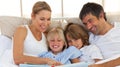 Joyful family reading a book on bed