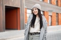 Joyful fashionable young woman with happy smile in stylish knitted hat in vintage spring coat in jeans in sweater walks outdoors Royalty Free Stock Photo