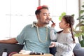 Joyful father playing with his little adorable daughter together, girl doing makeup to her dad by cosmetic, sitting on sofa in Royalty Free Stock Photo