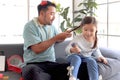 Joyful father playing with his little adorable daughter together, girl doing makeup to her dad by cosmetic, sitting on sofa in Royalty Free Stock Photo