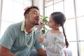 Joyful father playing with his little cute daughter together, girl doing makeup to her dad by cosmetic during sitting on sofa in Royalty Free Stock Photo