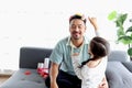 Joyful father playing with his little cute daughter together, girl doing makeup to her dad by cosmetic during sitting on sofa in Royalty Free Stock Photo