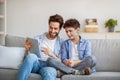 Joyful father and son using tablet computer, watching videos or playing online games, spending time together at home, Royalty Free Stock Photo