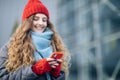 Joyful female in good mood typing and scrolling on smartphone outdoors. Curly-haired female using smartphone standing