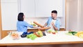 Joyful funny couple of handsome man and beautiful woman feeling playful while cooking at kitchen together. Royalty Free Stock Photo