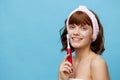 a joyful, funny woman stands in a white towel facing the camera holding a red toothbrush in her hand. Horizontal studio Royalty Free Stock Photo