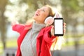 Joyful girl listening music and showing phone screen in winter