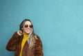 Joyful girl with long blond hair smiles. European girl in yellow sweater, faux fur coat and sunglasses. Autumn clothes