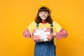 Joyful girl teenager in french beret, denim sundress holding red striped present box with gift ribbon isolated on yellow Royalty Free Stock Photo