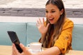 Joyful girl video calling friend on smart phone she greets with her hand. Young woman using phone camera for a chat with her Royalty Free Stock Photo