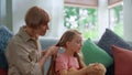 Joyful grandmother braiding little granddaughter hair at living room.