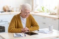 Joyful grey-haired senior woman using digital tablet in kitchen